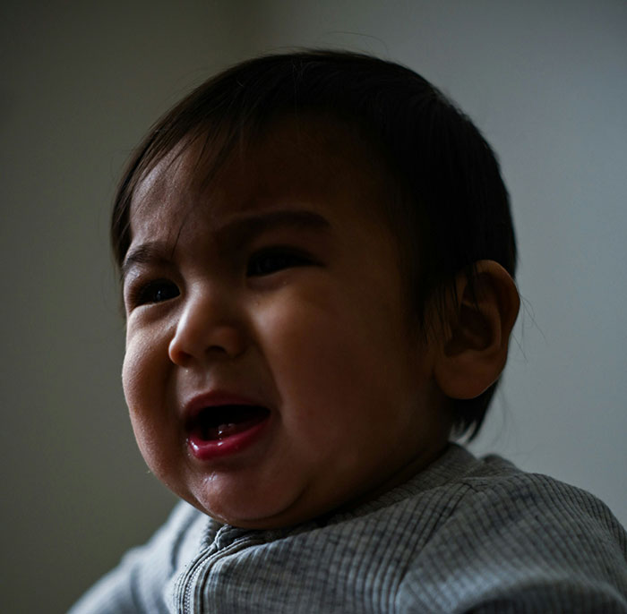 Close-up of a crying baby in a gray top. Medical professionals share patient stories that are not for the weak.