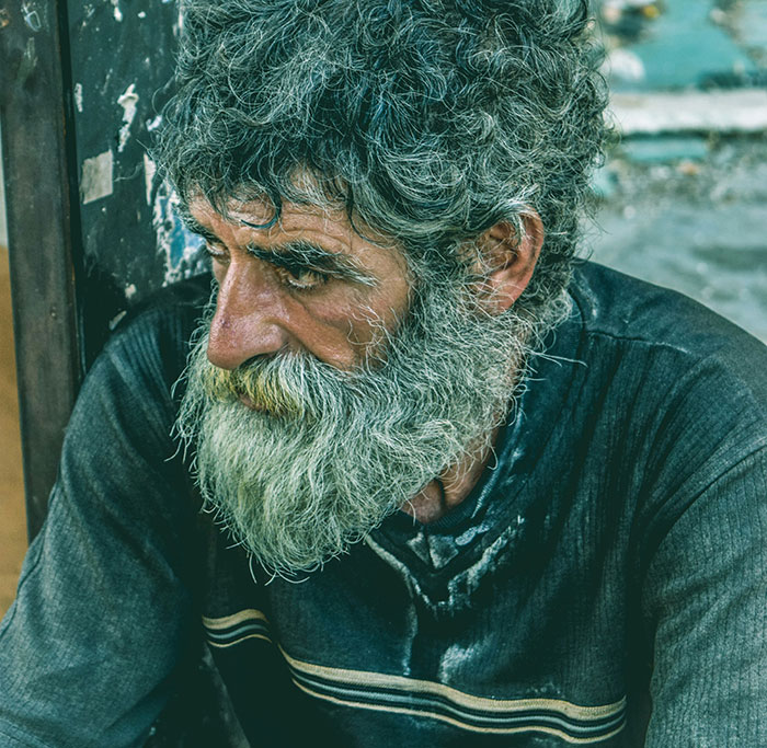 A man with a long gray beard and messy hair looks down, resembling a patient in a story not for the weak.