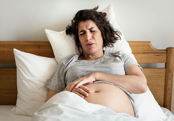 Pregnant woman experiencing pain in bed, reflecting patient stories.