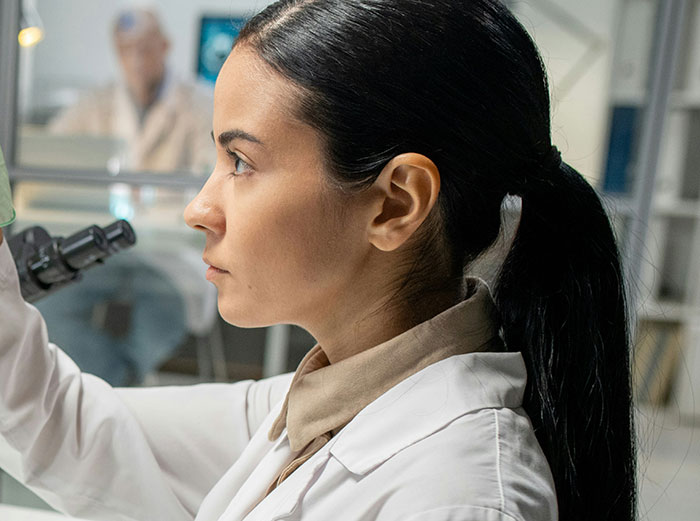 A medical professional looking intently at a microscope, with patient stories hinting at the challenging aspects of healthcare.