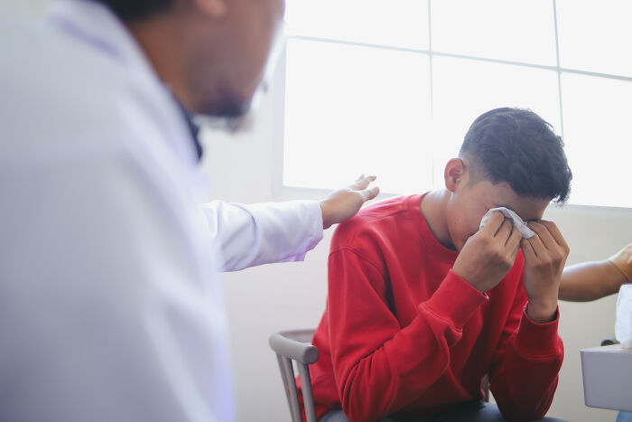 A person in a red shirt cries, holding a tissue, while another in a white coat offers comfort. Family secrets can be hard.