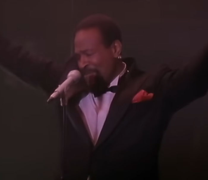 Male celebrity singer in a black tuxedo performing on stage with arms raised, related to disturbing celebrity facts.
