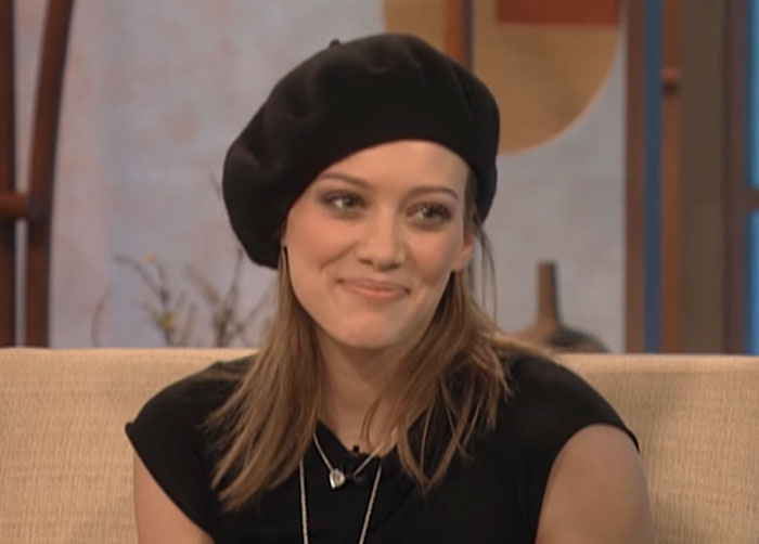 Young woman wearing a black beret and black shirt, smiling during a casual celebrity interview session.
