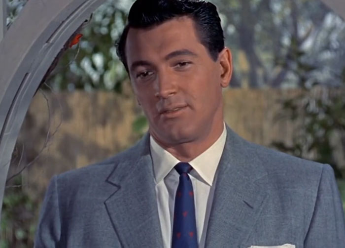 Classic male celebrity in a gray suit and tie standing near archway, related to disturbing celebrity facts and secrets.