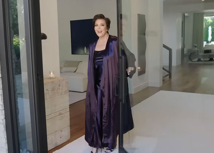 Woman in a dark satin outfit standing at a glass door in a modern home, related to disturbing celebrity facts.