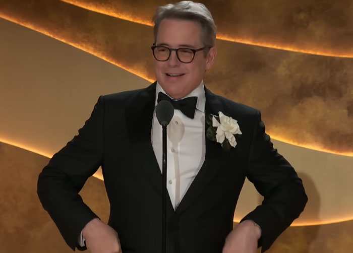 Man in a tuxedo with glasses speaking at a podium, illustrating disturbing celebrity facts for an award show.