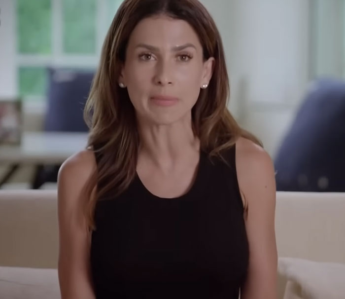 Woman with long brown hair wearing a black sleeveless top sharing disturbing celebrity facts in a bright indoor setting.