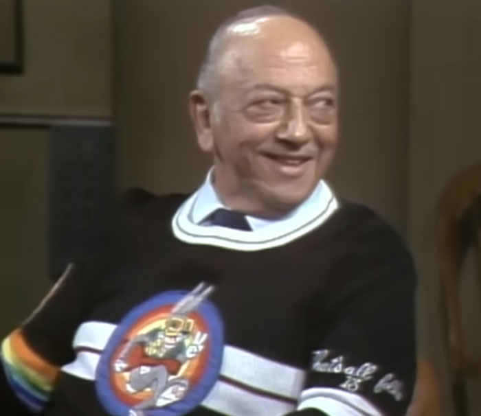 Elderly man smiling in a black sweater with a colorful graphic, related to disturbing celebrity facts topic.