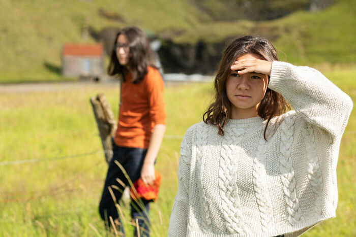 Teen girl shielding eyes in sunlight with another person blurred in background, reflecting on sickening and evil things parents say to kids