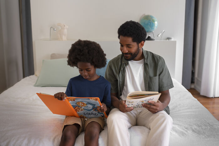 Father and son reading together on a bed in a bedroom, illustrating parent-child interaction and communication.