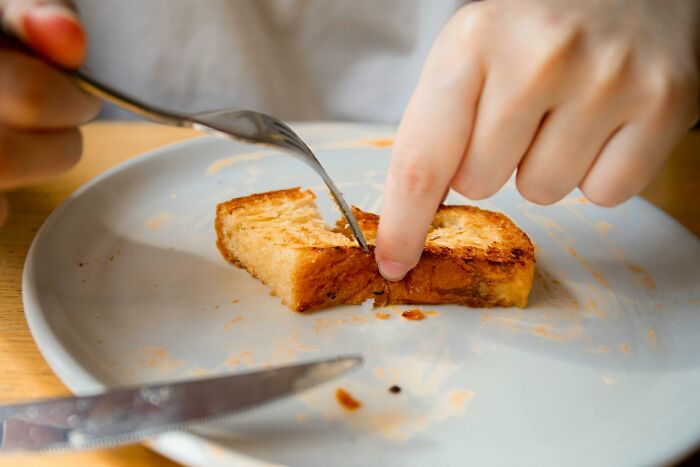 Close-up of a person's hand cutting toast on a white plate, illustrating sickening and evil parenting moments.