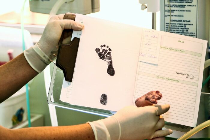 Medical professional holding a newborn's footprint and fingerprint during a hospital procedure related to parent and child care.