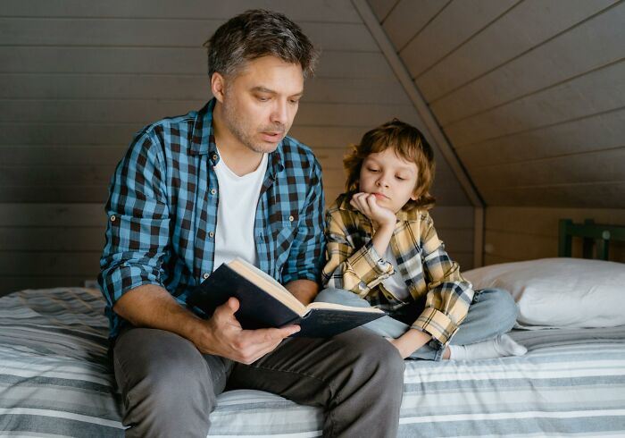 Father reading a book to his child on a bed, illustrating moments of parents telling kids sickening and evil things.