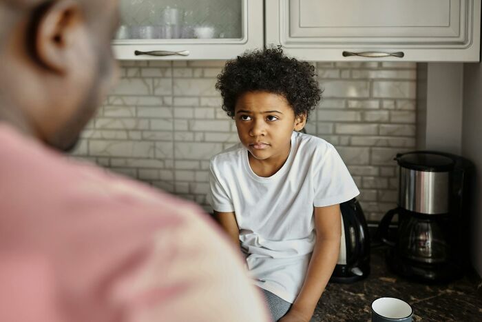 Child sitting on kitchen counter looking upset while parent speaks, illustrating sickening and evil things parents tell kids.
