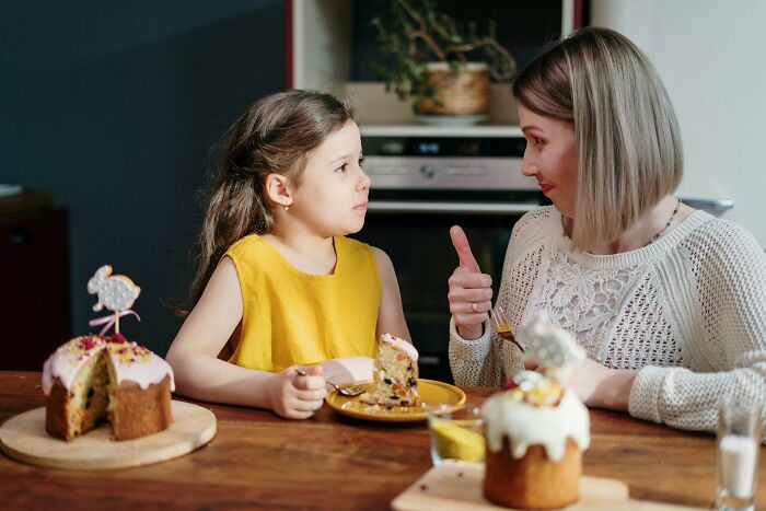 Mother giving a thumbs up while talking to her daughter about cake, reflecting on horrible things parents have told kids.