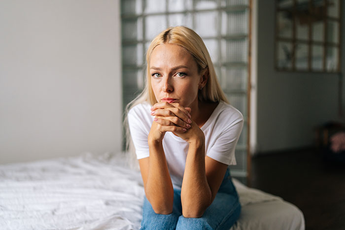 Woman with blonde hair sitting on bed, looking pensive, reflecting on confusing and wild family dynamic issues.