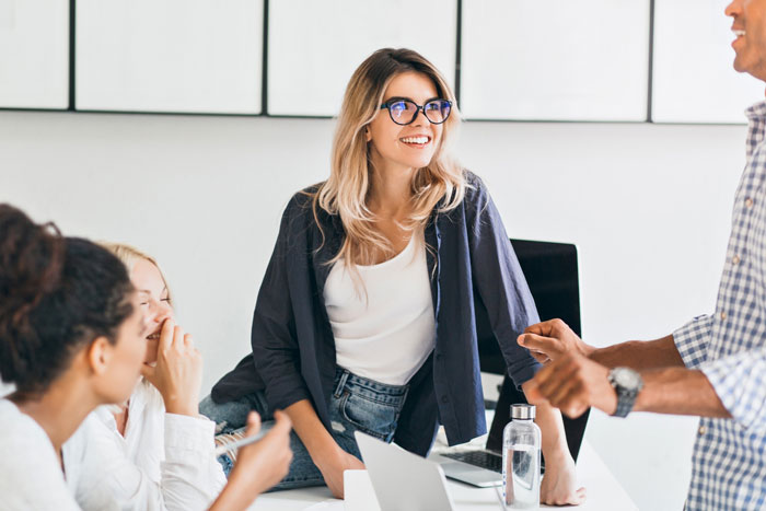 Young woman boasting at a casual office meeting while coworkers react, highlighting a cheater lady and animal-lover coworker tension.