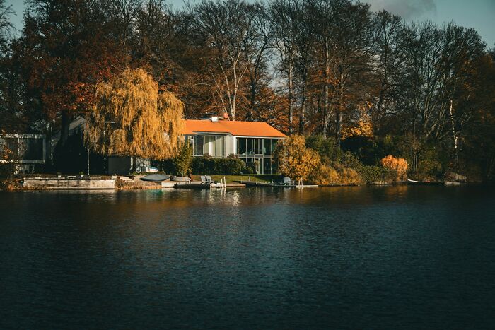 Lakefront house surrounded by autumn trees under a cloudy sky, illustrating peaceful karma moments in nature.