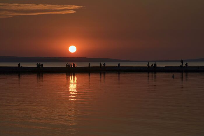 Silhouettes of people on a pier during a vibrant sunset, reflecting on the water. A gentle reset button for your day.