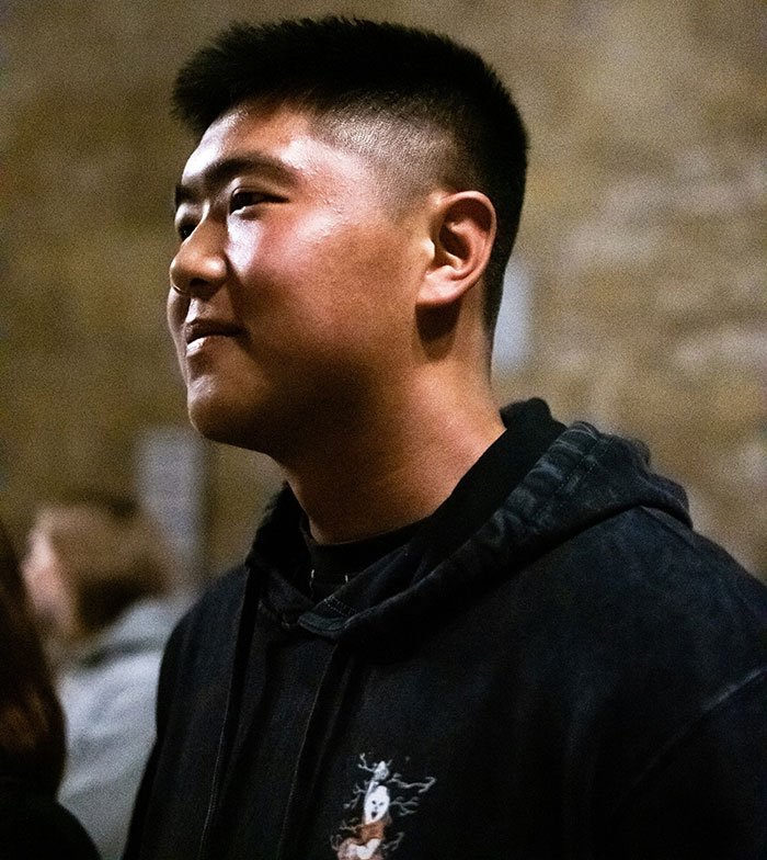 Young man with a short haircut wearing a hoodie, reflecting on amusing Chinese and Japanese tattoo translations.