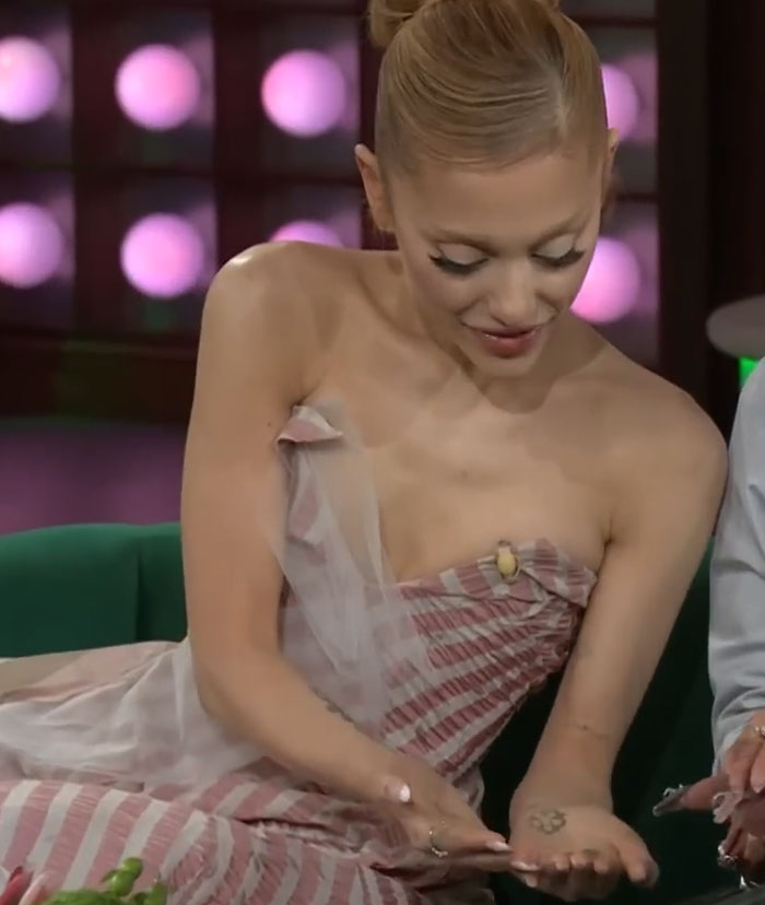 Woman showing a small intricate tattoo on her forearm while sitting on a green couch in a studio setting