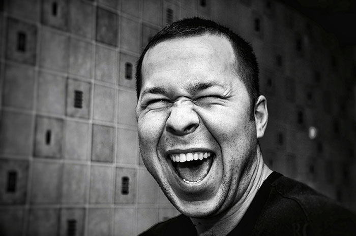 Close-up of a man laughing heartily, illustrating amusement often felt by people who know Chinese and Japanese about tattoos.