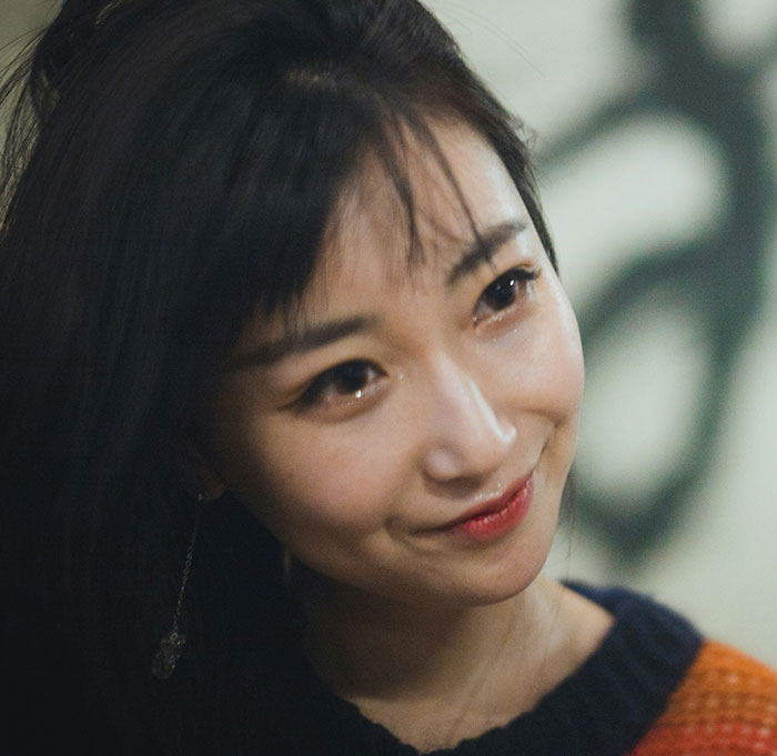 Young woman smiling warmly, showcasing intricate tattoos with Chinese and Japanese characters, amusing language experts.