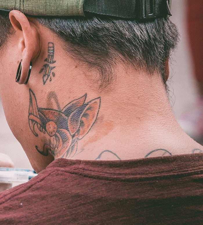 Person with neck and ear tattoos featuring Chinese and Japanese characters and a colorful animal design on the neck.