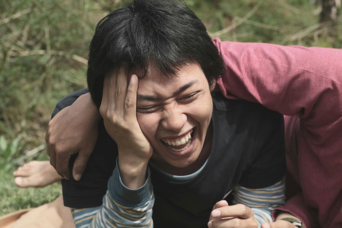 Young person laughing joyfully outdoors, capturing the amusement of people who know Chinese and Japanese tattoos.