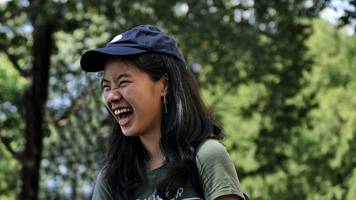 Young woman laughing outdoors, exemplifying amusement by people who know Chinese and Japanese tattoos.