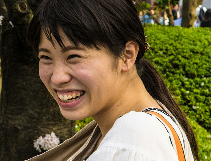 Smiling young woman outdoors surrounded by greenery, capturing the amusement of people who know Chinese and Japanese tattoos.