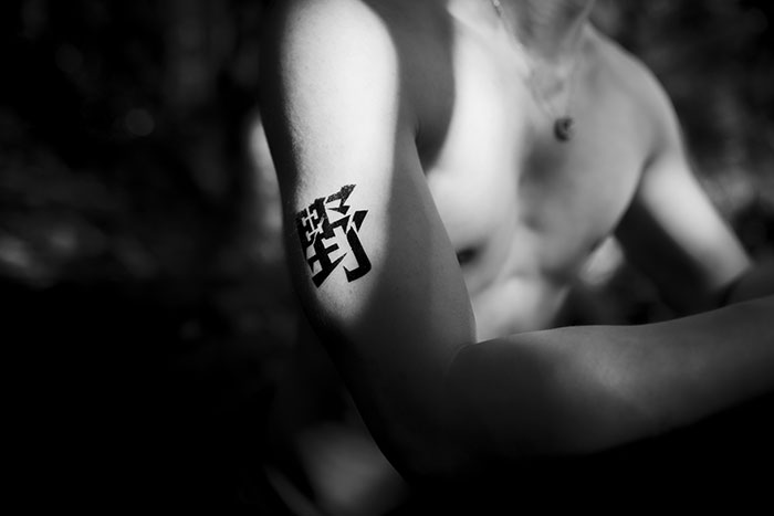 Black ink Chinese tattoo on a shirtless man's upper arm, highlighting humorous or mistaken tattoo meanings.