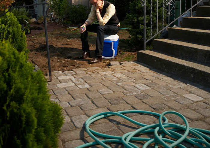 Man sitting on a cooler looking frustrated in a garden, illustrating coworker stupidity in a work or outdoor setting.