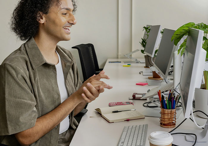 Coworker smiling at computer screen in office, surrounded by notebooks, stationery, and coffee, showcasing quirky coworker moments.