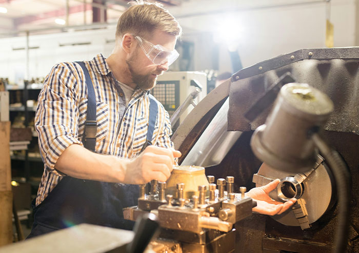 Man wearing safety glasses and plaid shirt operating machinery in a workshop, showcasing coworker workplace actions.