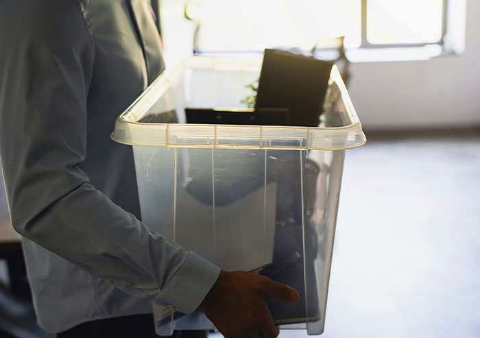 Person holding an empty plastic bin with office items inside, illustrating coworkers who took stupidity to new heights.