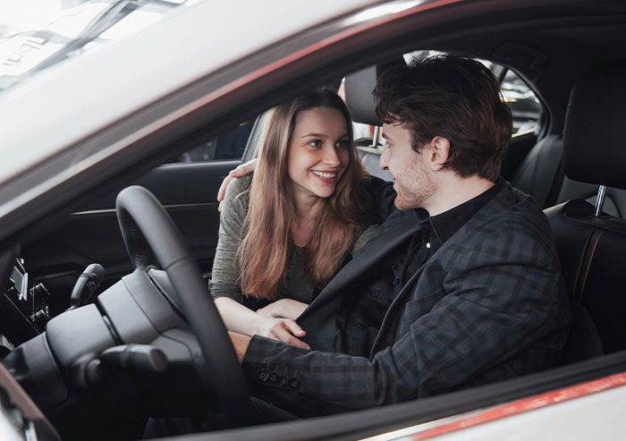 Two coworkers sharing a laugh inside a car, illustrating moments of humor among coworkers who took stupidity to new heights.