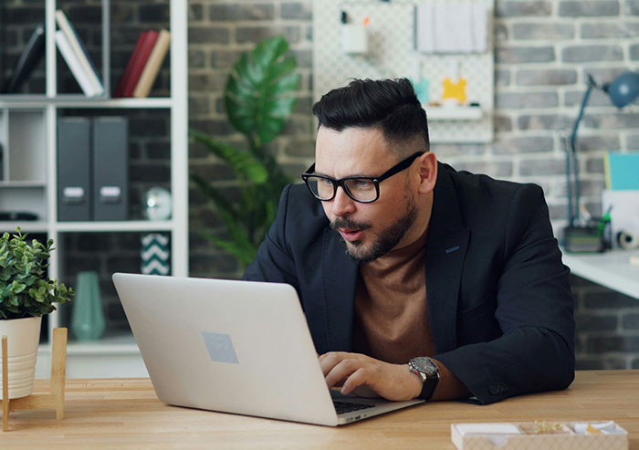 Man with glasses working on laptop in office, illustrating coworker interactions and moments of workplace stupidity.
