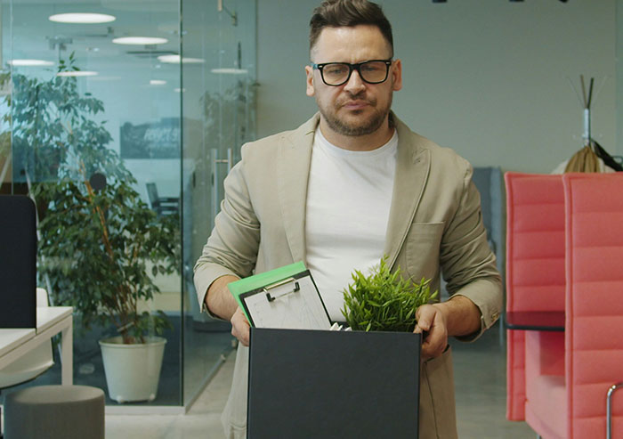 Man holding box with office items looking frustrated, illustrating coworkers who took stupidity to new heights.