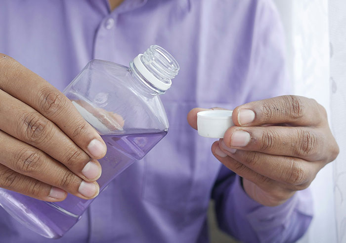 Close-up of coworker pouring purple liquid from a plastic bottle into the cap, showcasing workplace mistakes and carelessness.