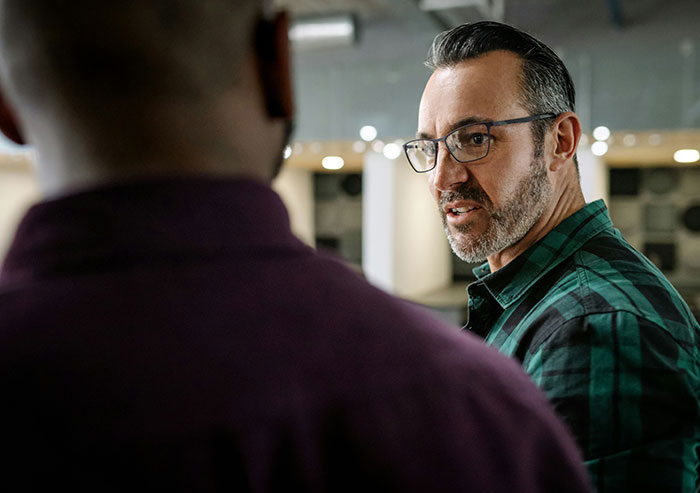 Two coworkers in conversation, one wearing glasses and a green plaid shirt, illustrating workplace interactions and coworker dynamics.