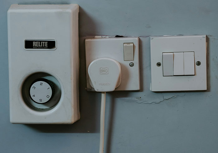 Old white electrical timer and switches mounted on a wall, illustrating coworker stupidity with dangerous DIY electrical setup.