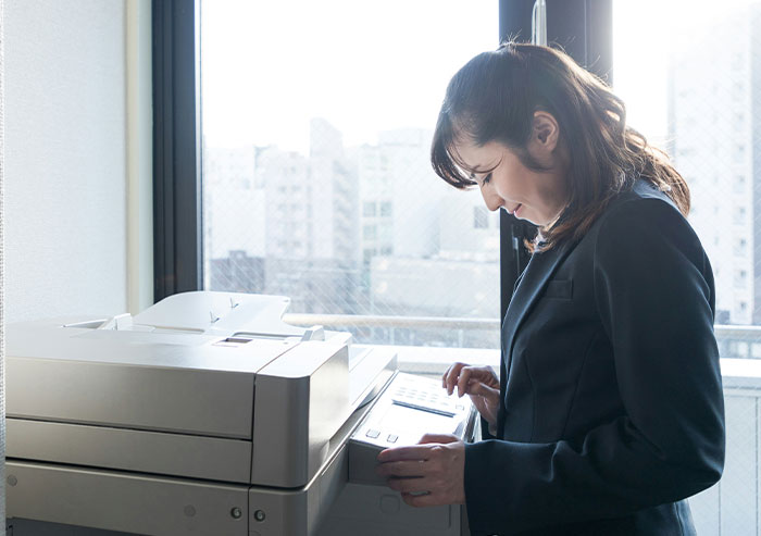 Woman in business attire struggling with office copier, highlighting coworker office mistakes and workplace blunders.