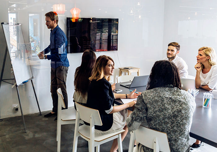 Team of coworkers in a bright office having a discussion during a brainstorming session with a whiteboard and laptop.