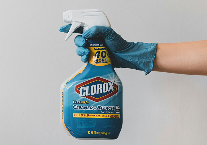 Hand in blue glove holding Clorox cleaner spray bottle representing coworkers who took stupidity to new heights with cleaning mistakes.