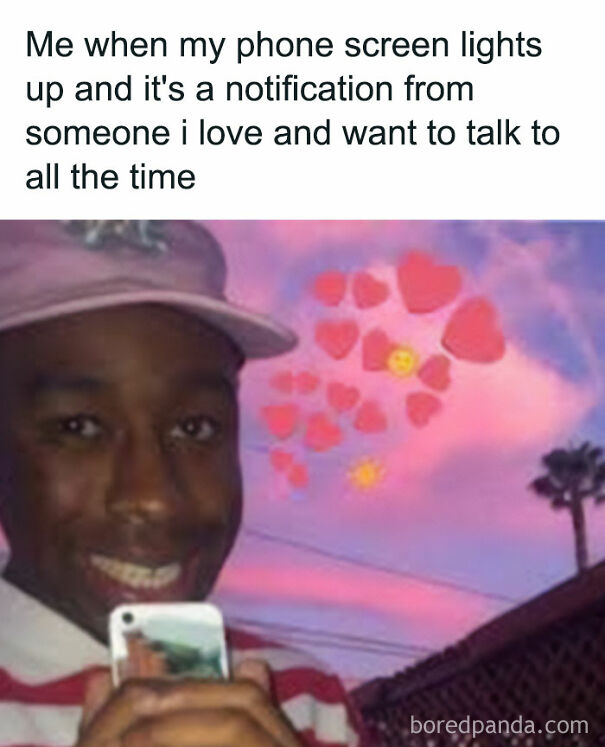 A wholesome post shows a smiling person holding a phone, with floating hearts and emojis against a pink sky.