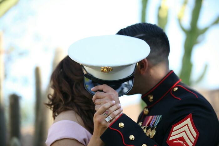 Couple at a wedding holding hands while the groom in military dress uniform hides their faces during a ceremony.