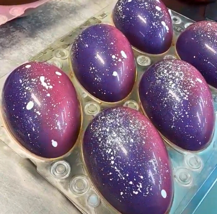 Galaxy marbled Easter eggs with purple and pink hues, featuring white speckles, displayed in an egg carton for creative DIY decor.