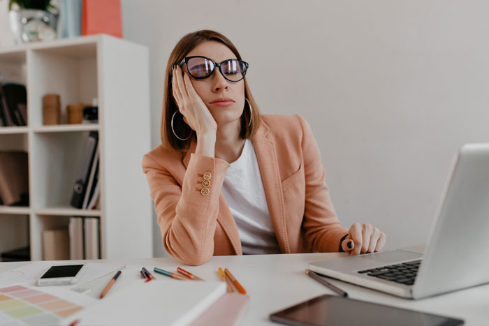 Woman in office wearing glasses, resting head on hand, looking disappointed during company staff celebration with balloons and lunch