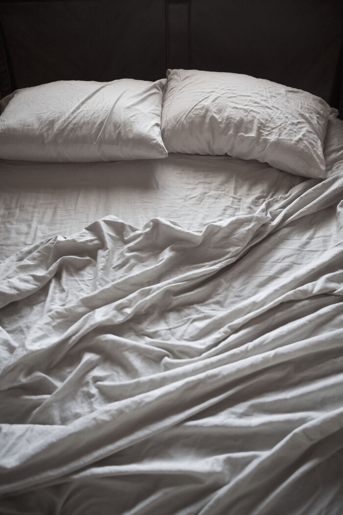 A messy, unmade bed with wrinkled white sheets and two pillows. A visual representing being cheated on.